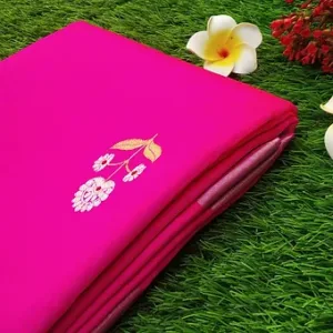 Folded pink pure silk Chanderi saree featuring delicate white floral butta embroidery near the pallu and a soft silver zari border, placed on green grass with decorative flowers.