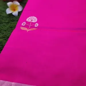 Close view of a bright pink pure silk Chanderi saree featuring delicate white floral butta embroidery near the pallu and a subtle silver zari border, displayed on a grass background with a plumeria flower.